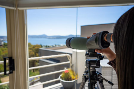 Girl using binoculars on a balcony in a city next to the sea, seaside town in hobart AUSTRALIA bird watchingの写真素材