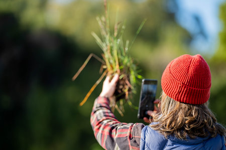 regenerative organic female farmer, taking soil samples and looking at plant growth in a farm. practicing sustainable agriculture. Taking a photo with her phone in australiaの写真素材