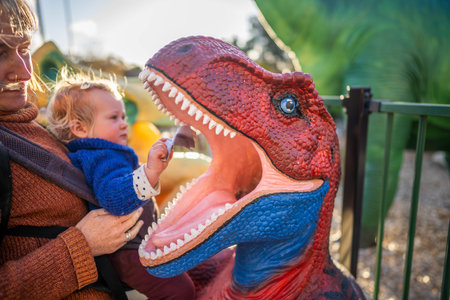 Mother and child looking at dinosaur model in the park on a sunny dayの写真素材