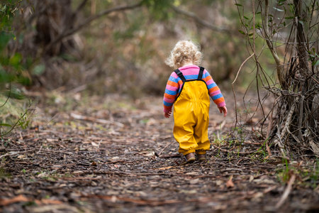 baby walking in a park in yellow overalls in the bushの写真素材