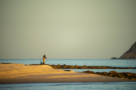 beach fishing in the ocean waves at dusk on a holiday in summerの写真素材