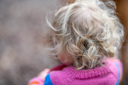 Little girl with blonde curly hair in pink sweater and blue jeans.