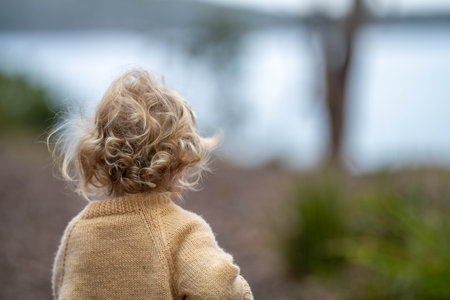 Back view of a little girl with curly hair looking at the sea