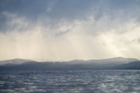 soft beautiful rays over the water through clouds over an island at dawn with pink clouds and the...