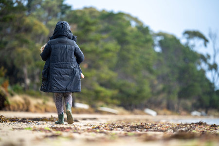 mother and baby playing on the beach. toddler in overalls walking and playing with sand and dogs on the seasideの写真素材