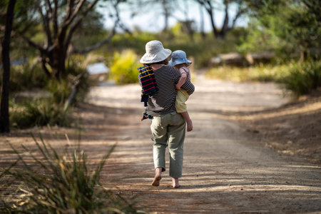 Mother with baby in a carrier on her chest on a hike, taking a bush walk in Summer in a parkの写真素材