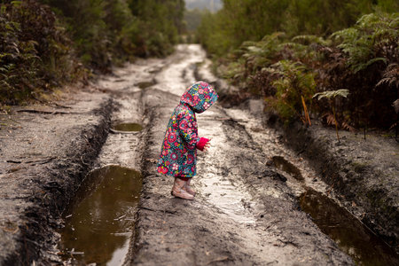 Little girl in raincoat playing in muddy puddle in tropical rainforest