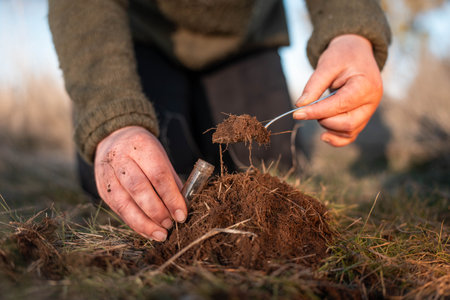 farmer collecting soil samples in a test tube in a field. Agronomist checking soil carbon and plant health on a farm with a microscope soil testの写真素材