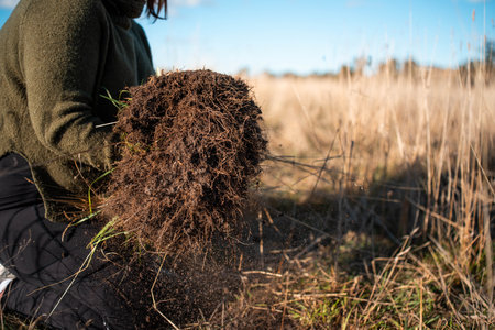 A young female farmer is digging a field with a pile of freshly dug grass.