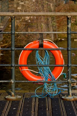 an orange old tatty life preserve secured to railings on a wooden river jetty.の写真素材