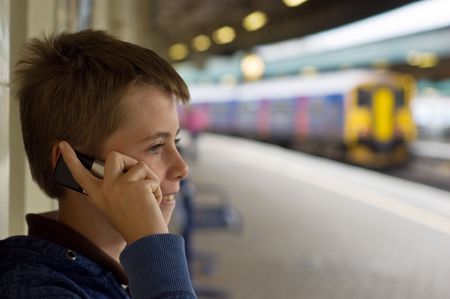 a teenage boy laughing and talking on a mobile phone at a train station.の写真素材