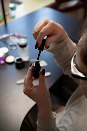 Girl in protective glasses opens dark nail polish near manicure tools on dark backgroundの写真素材