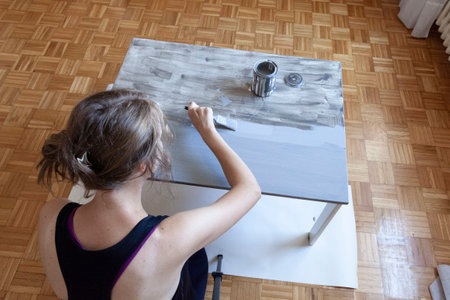 Woman in black shirt painting old white wooden table in light grey color at homeの写真素材