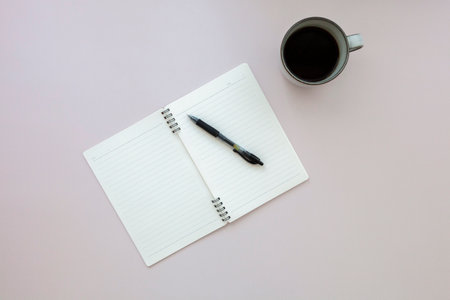 Top view of empty notebook with pen near cup of black coffee on pink backgroundの写真素材
