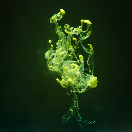 Yellow ink in water in a shape of clouds. Colorful ink and paint swirling underwater on dark...