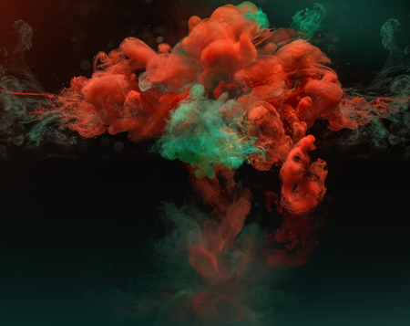 Red and green complementary colors in clouds. Colorful ink and paint swirling underwater on dark background.の写真素材
