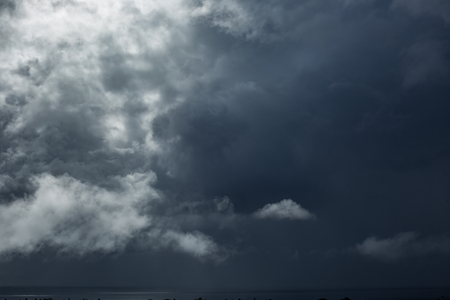 Dramatic dark storm clouds over the ocean water with bright spot of lightの写真素材