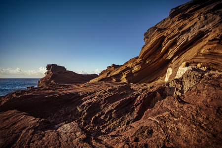 Sharp shapes, volcanic beach shorline, wind shaped layered rocks and stones, Aeolian process in wild nature, ocean water with wavesの写真素材