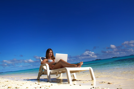 Beautiful girl on tropical beach getting tan and working with laptopの写真素材