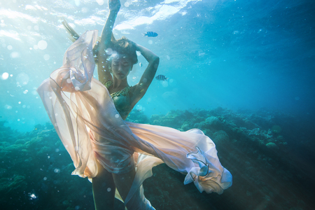 Beautiful girl in fashion dress posing underwater on coral reef on water backgroundの写真素材