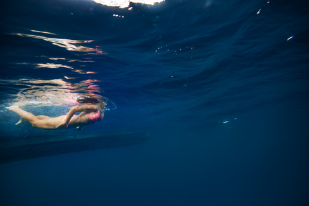 Girl in pink bikini underwater near bottom of a boat. Copy space on right side of image with blue...