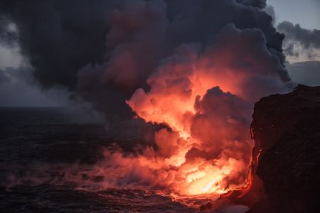 Hot bright lava streams flowing into the ocean making big clouds of steam against sunset sky on backgroundの写真素材