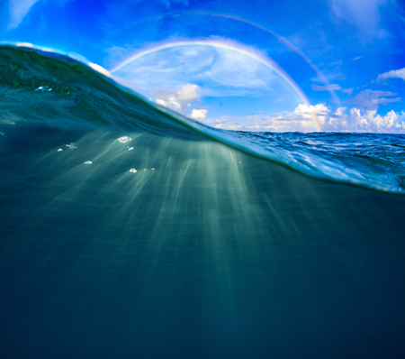 A rainbow in the sky and sea water splitted by waterline with deep blue backgroundの写真素材