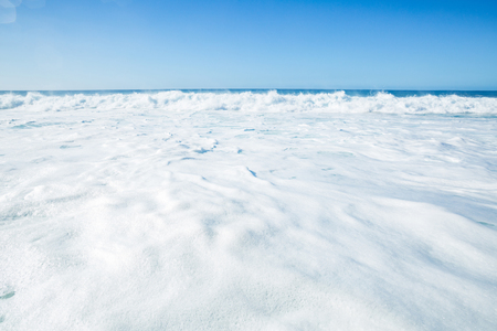 White shorebreak foam upcoming to a shore. Seascape with bright backgroundの写真素材