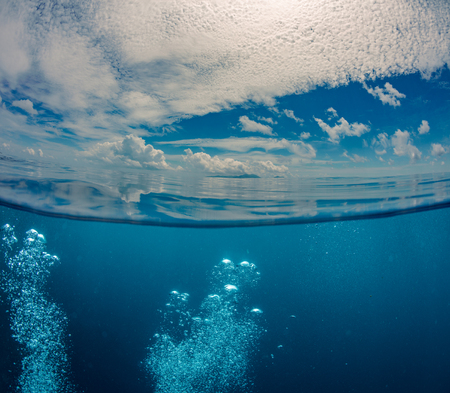 Peaceful sea background with calm reflected water, rich clouds and air bubbles underwaterの写真素材