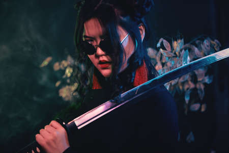 Oriental style girl with katana sword on dark smoky background in shallow depth of fieldの写真素材