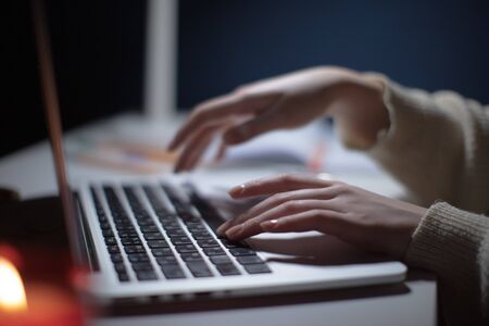 Closeup hands of A girl working on laptop on white table at night, side view, shallow depth of field