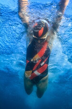 Professional swimmer moving fast in ocean water broght blue color on background, underwater shotの写真素材