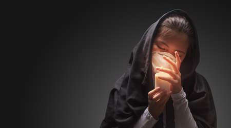 Mourning woman wearing black cloth holding candle with fire, the expression of deep sorrow for someone who has died during pandemicの写真素材