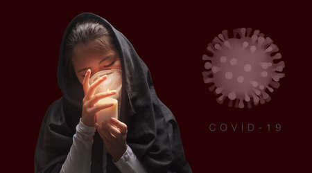 Mourning woman wearing black cloth holding candle with fire, the expression of deep sorrow for someone who has died during pandemicの写真素材