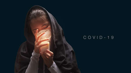 Mourning woman wearing black cloth holding candle with fire, the expression of deep sorrow for someone who has died during pandemicの写真素材