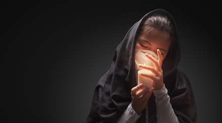 Mourning woman wearing black cloth holding candle with fire, the expression of deep sorrow for someone who has died during pandemicの写真素材