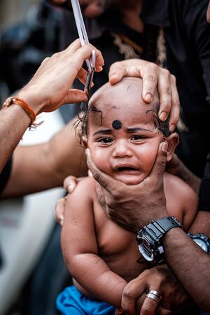 Close-up of baby boy devotee getting tonsured or head shaving ritual in Thaipusam Festival.