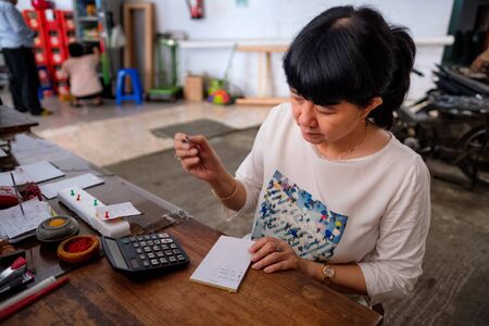 Asian Indonesian women, the owner of small local family-owned business store, or locally called warung, calculating profit by her desk. Selective Focus.の写真素材