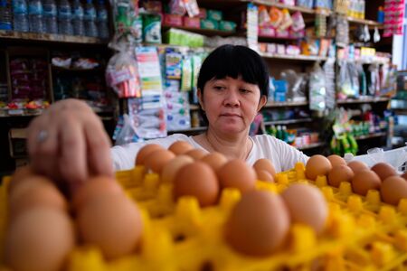 Asian Indonesian women arranging eggs inside small local family-owned business store, or locally called warung. Location is in Tasikmalaya, Indonesia. Selective Focus.の写真素材