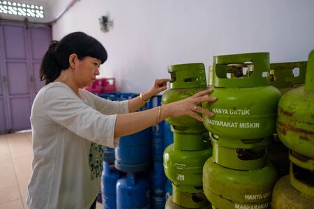 Asian Indonesian women arranging 3Kg gas cylinders inside small local family-owned business store, or locally called warung. The translation of the text is 'only for the poor'. Selective Focus.の写真素材