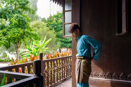 Malay man are wearing traditional cloth and adjusting his samping songket at traditional wooden house.の写真素材
