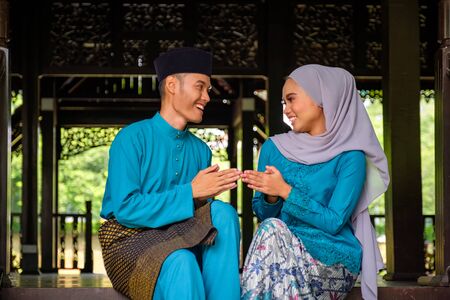 Young couple of malay muslim in traditional costume shaking hand during Aidilfitri celebration at...