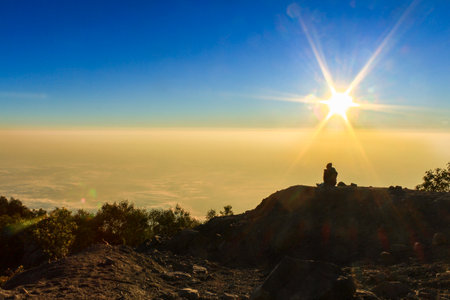 Silhouette of a Person Watching Sunrise on Mountain Summit with Sun Flare