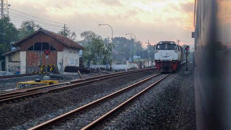Indonesian Train Passing Through Railway Tracks at Sunset in a Small Townの写真素材