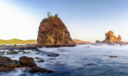 Dramatic Seaside Landscape with Long Exposure, Smooth Wave, Rocks and Sunset in Yogyakarta, Indonesiaの写真素材