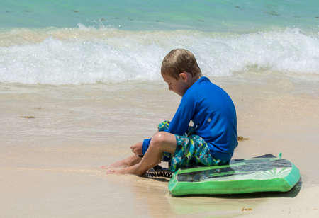 blonde kid sitting on surfboard in the beach
