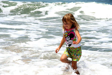 portrait of a little girl running in the waves at the beachの写真素材