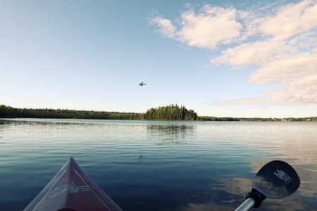 A floatplane takes off from a lake while a lone kayaker stops to watchのeditorial素材