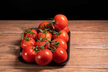 Many fresh red tomatoes with stem on a tray from supermarket on wooden tableの写真素材