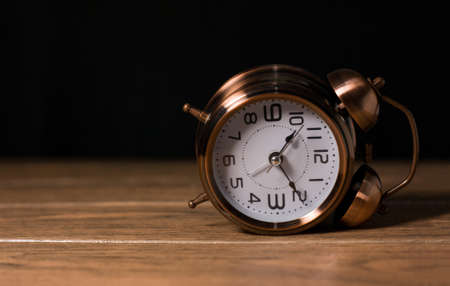 Old antique analogy alarm clock metallic steel fallen sideways in a wooden table with black backgroundの写真素材